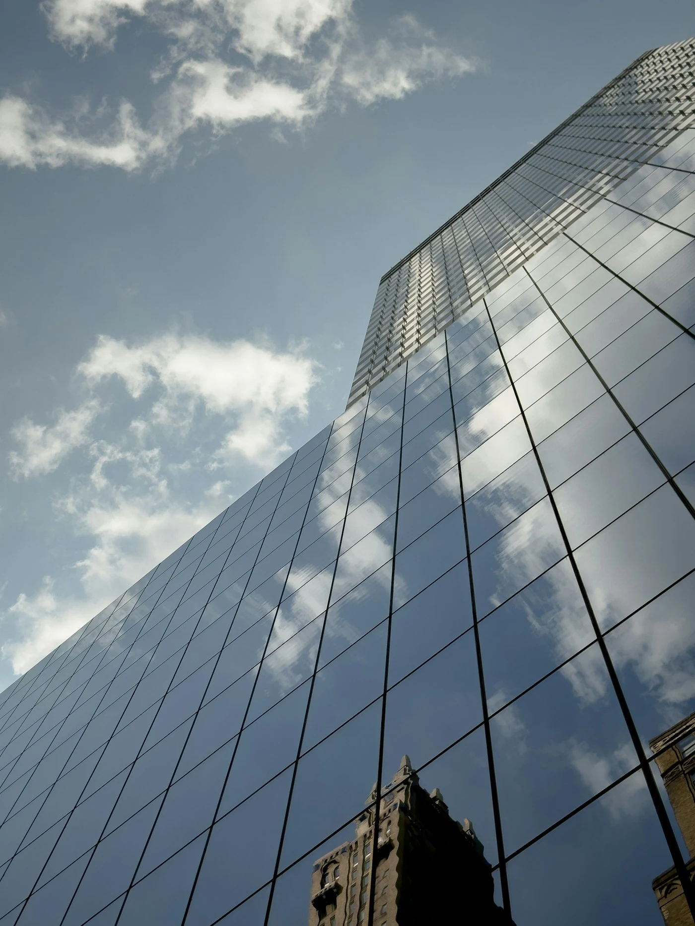 Fachada de vidro refletindo edifícios e céu com nuvens