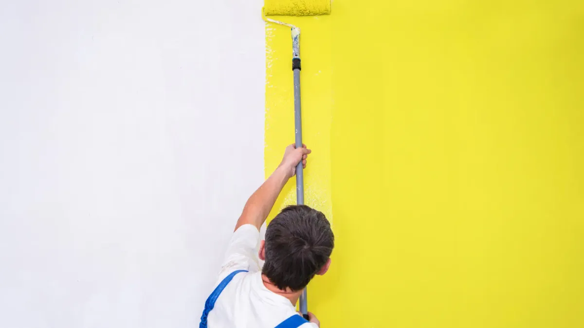Profissional pintando parede amarela com rolo de cabo longo
